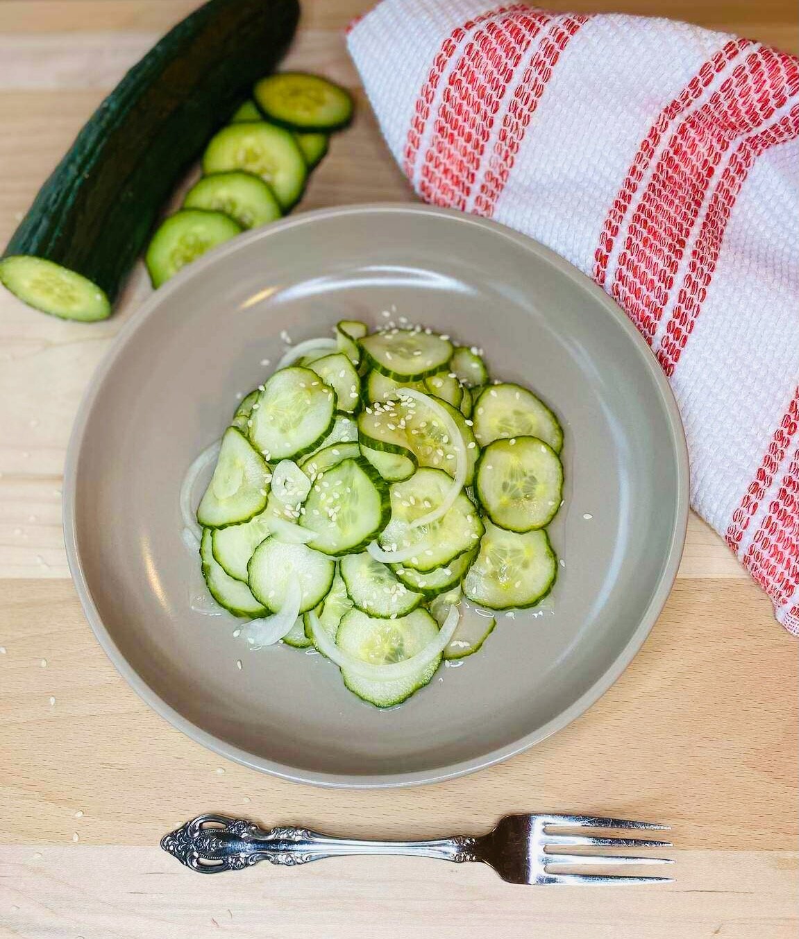 A bowl of marinated cucumbers with a towel, and fork beside the bowl.