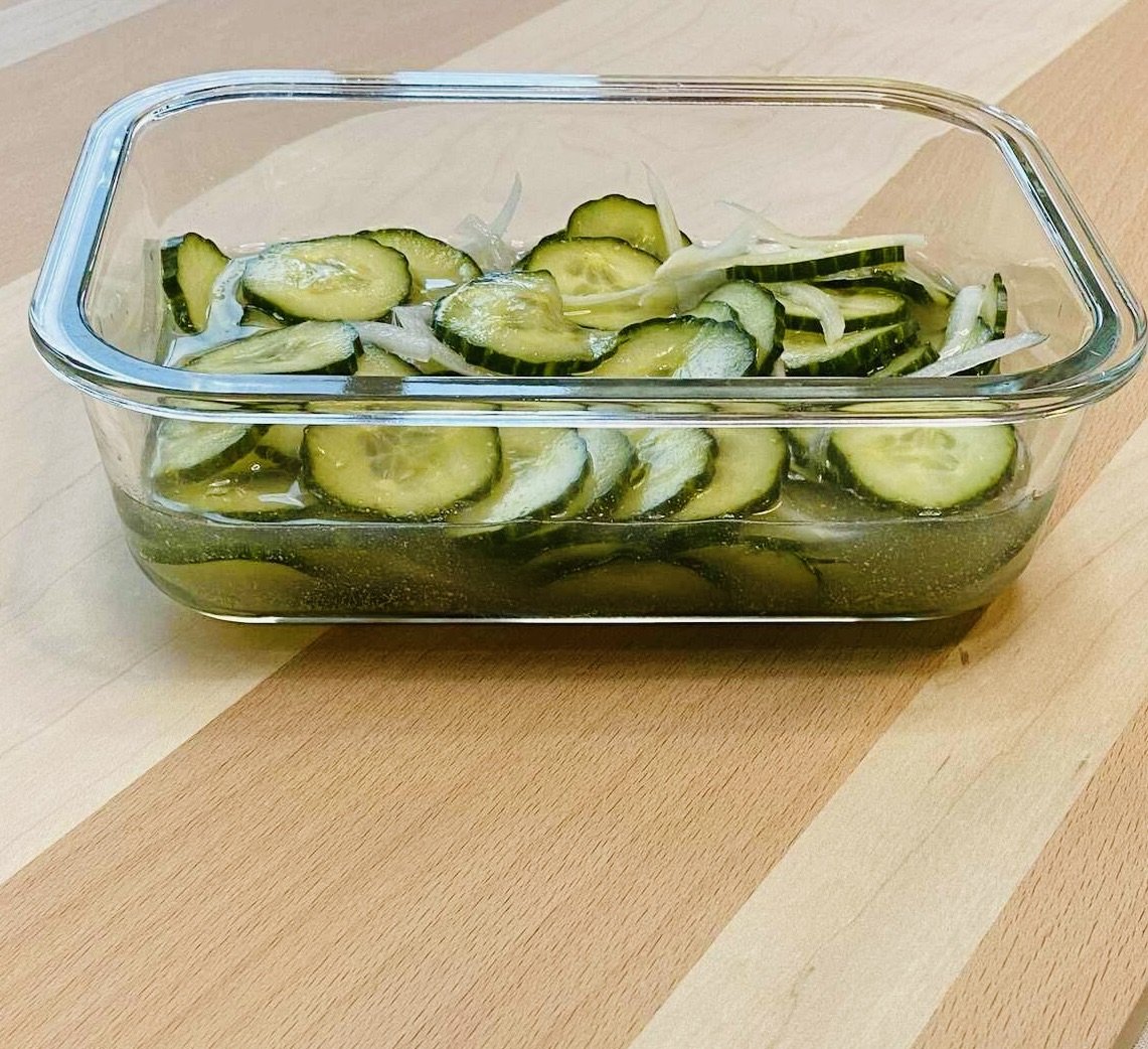 Sliced cucumbers marinating in a glass dish.