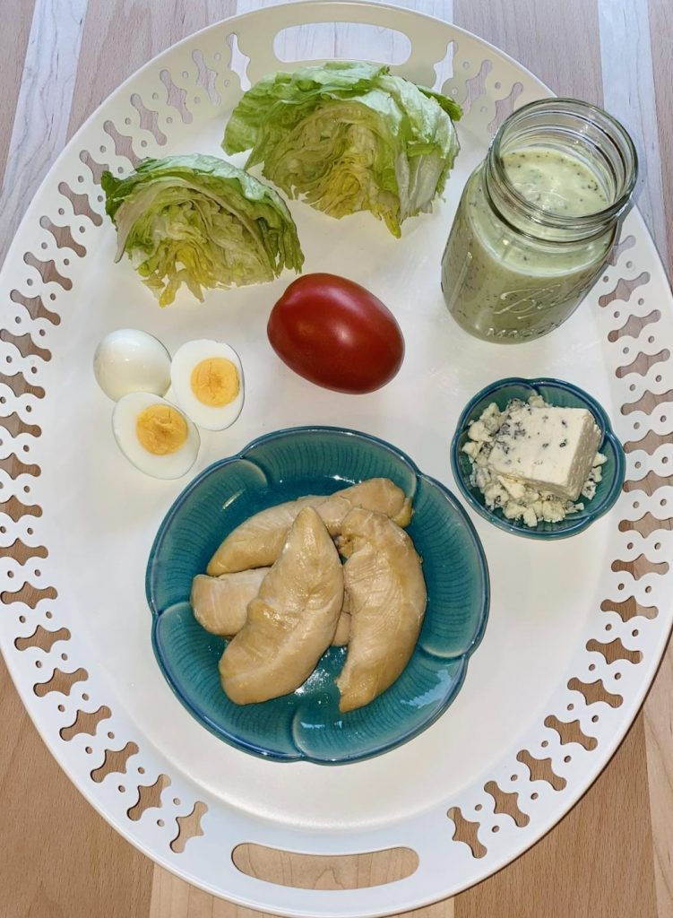 White tray with all the ingredients to make the salad including lettuce, tomato, egg, chicken, cheese and dressing.