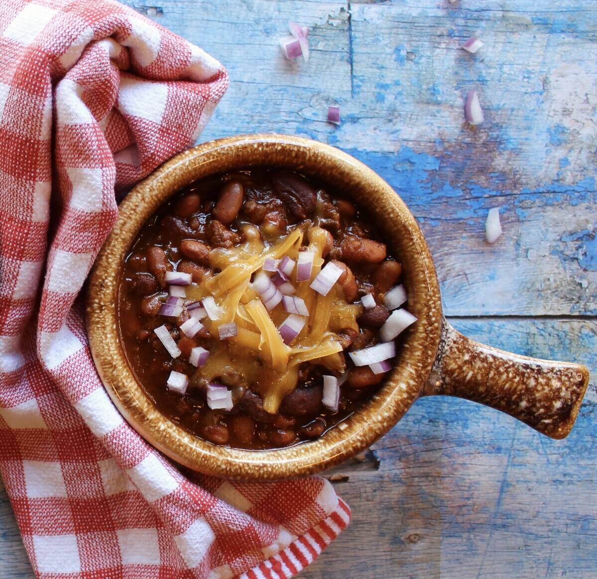 bowl of chili with cheese and onions beside a towel.