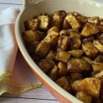 Orange dish of seasoned and roasted potatoes beside a white napkin.