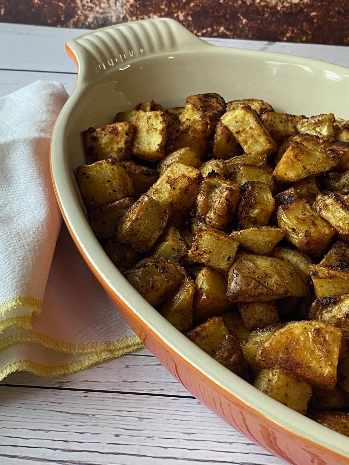 Orange dish of seasoned and roasted potatoes beside a white napkin.