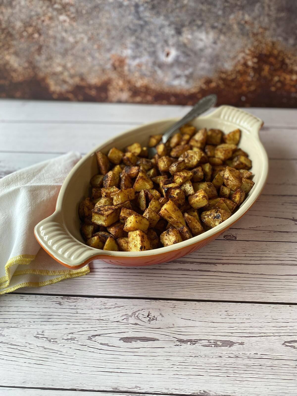 Orange dish of roasted potatoes with a spoon and a napkin