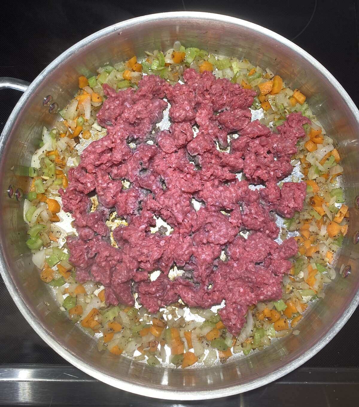 Fry pan with cooked vegetables and ground beef.