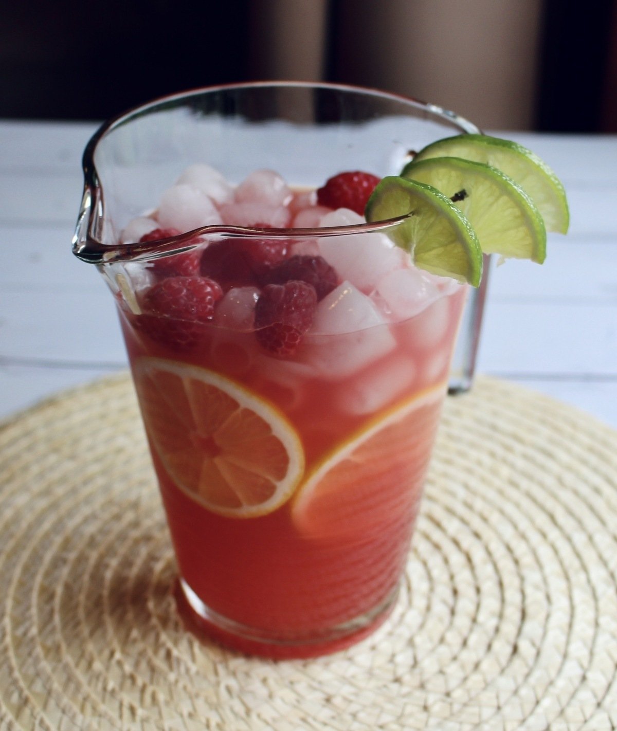 A full pitcher of mocktail with ice, floating fruit, and lime garnish.