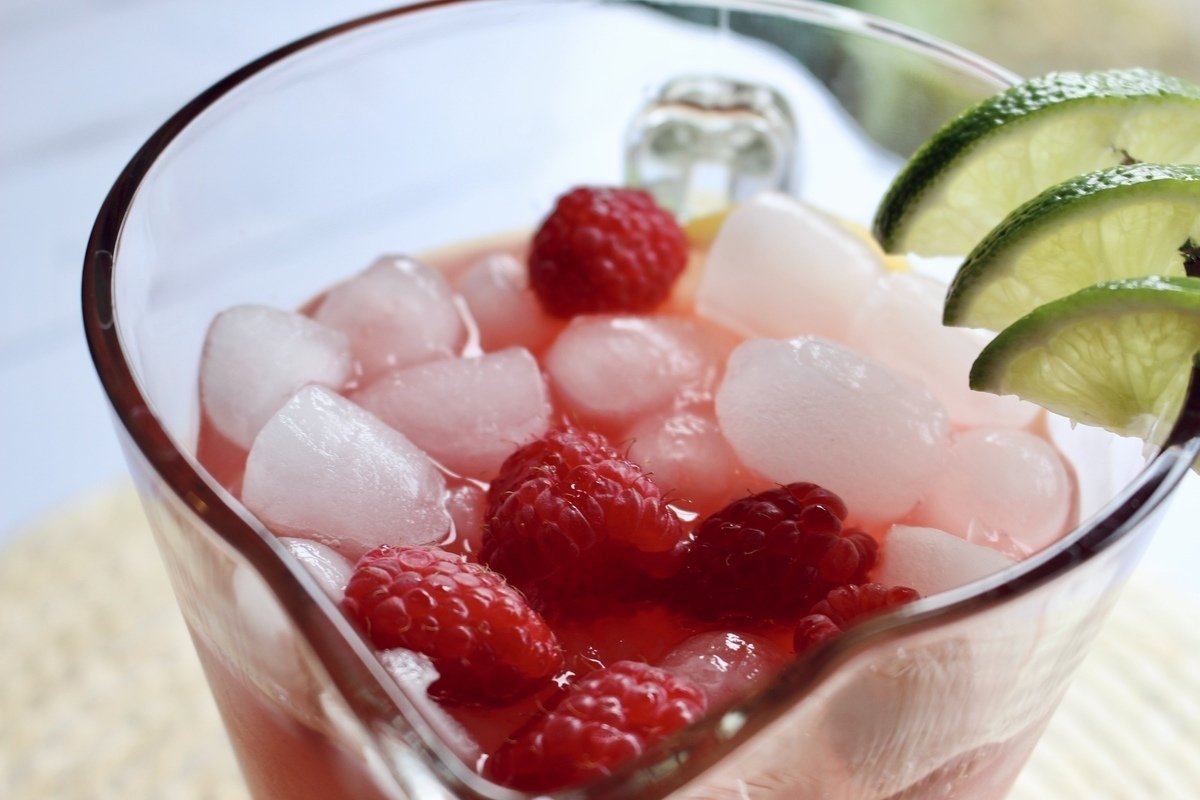 Top of pitcher of punch with lime garnish, ice and raspberries.