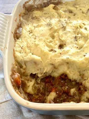 A casserole dish with shepherds pie with a scoop spooned out.