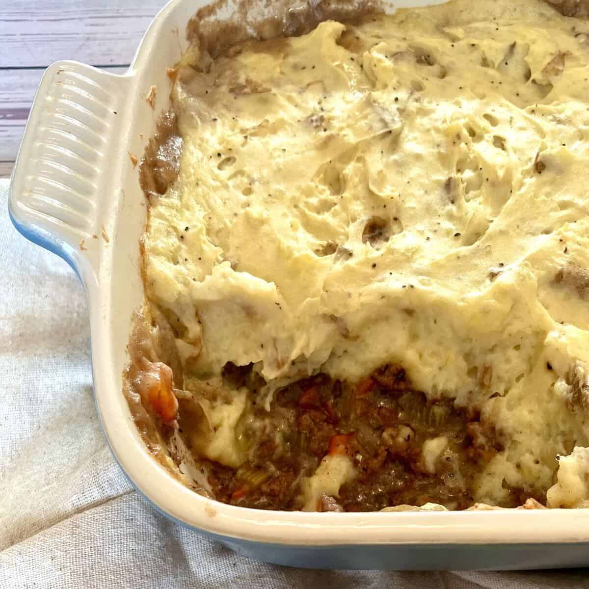 A casserole dish with shepherds pie with a scoop spooned out.