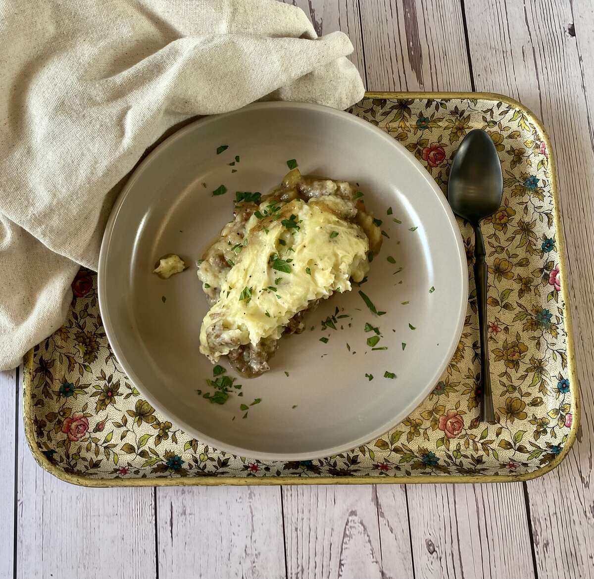 A serving of shepherds pie on a plate on a tray with a spoon and napkin.