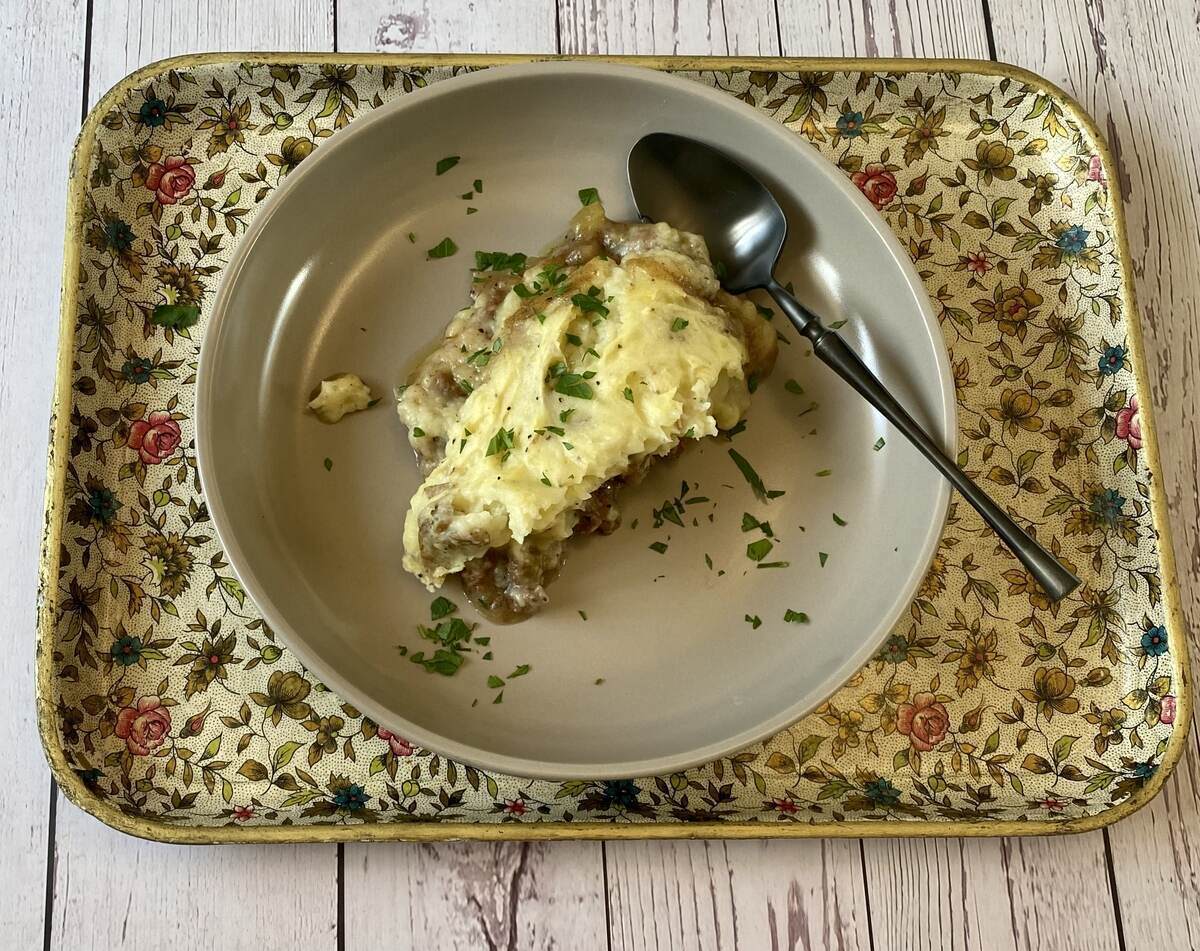 Serving of shepherds pie on a plate on a tray with a spoon.