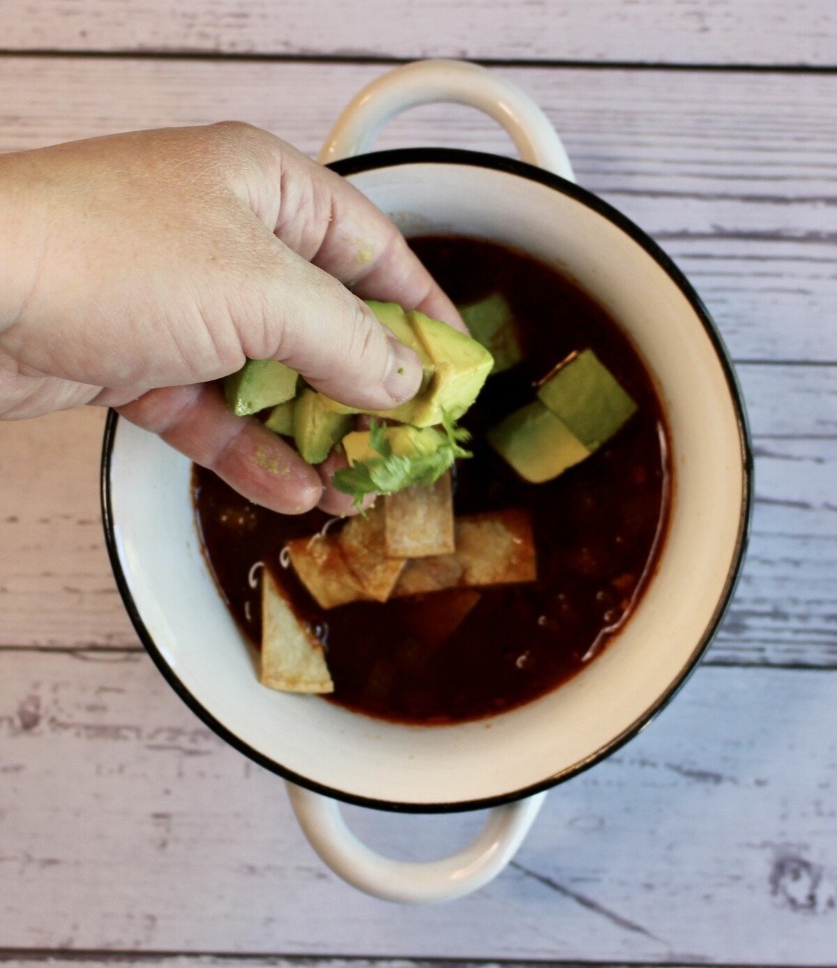 a bowl with soup and adding avocado chunks.