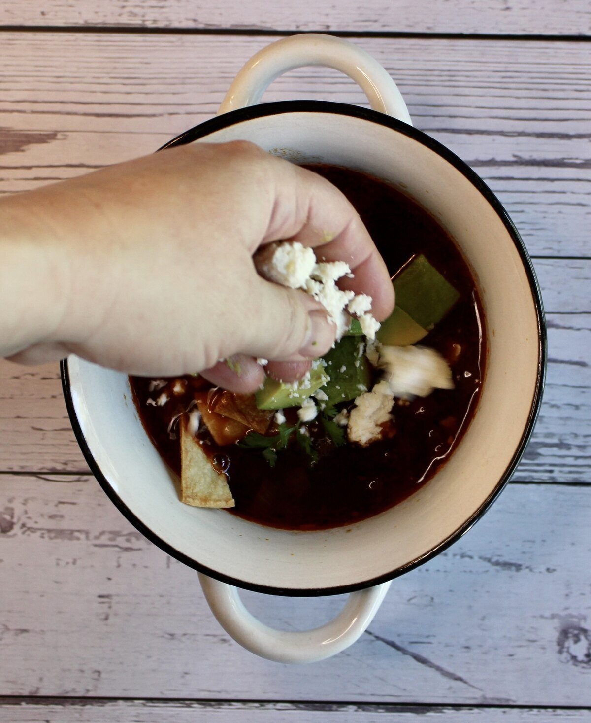 A bowl of soup and adding queso fresco crumbles.