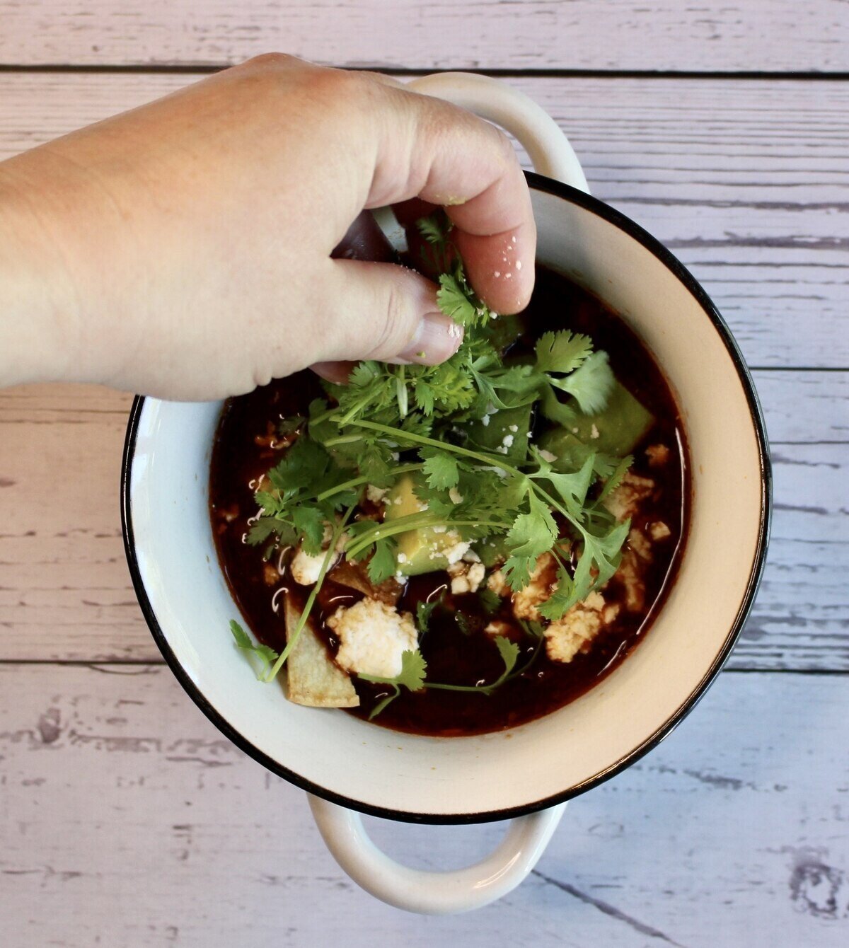 Topping a bowl of tortilla soup with cilantro.