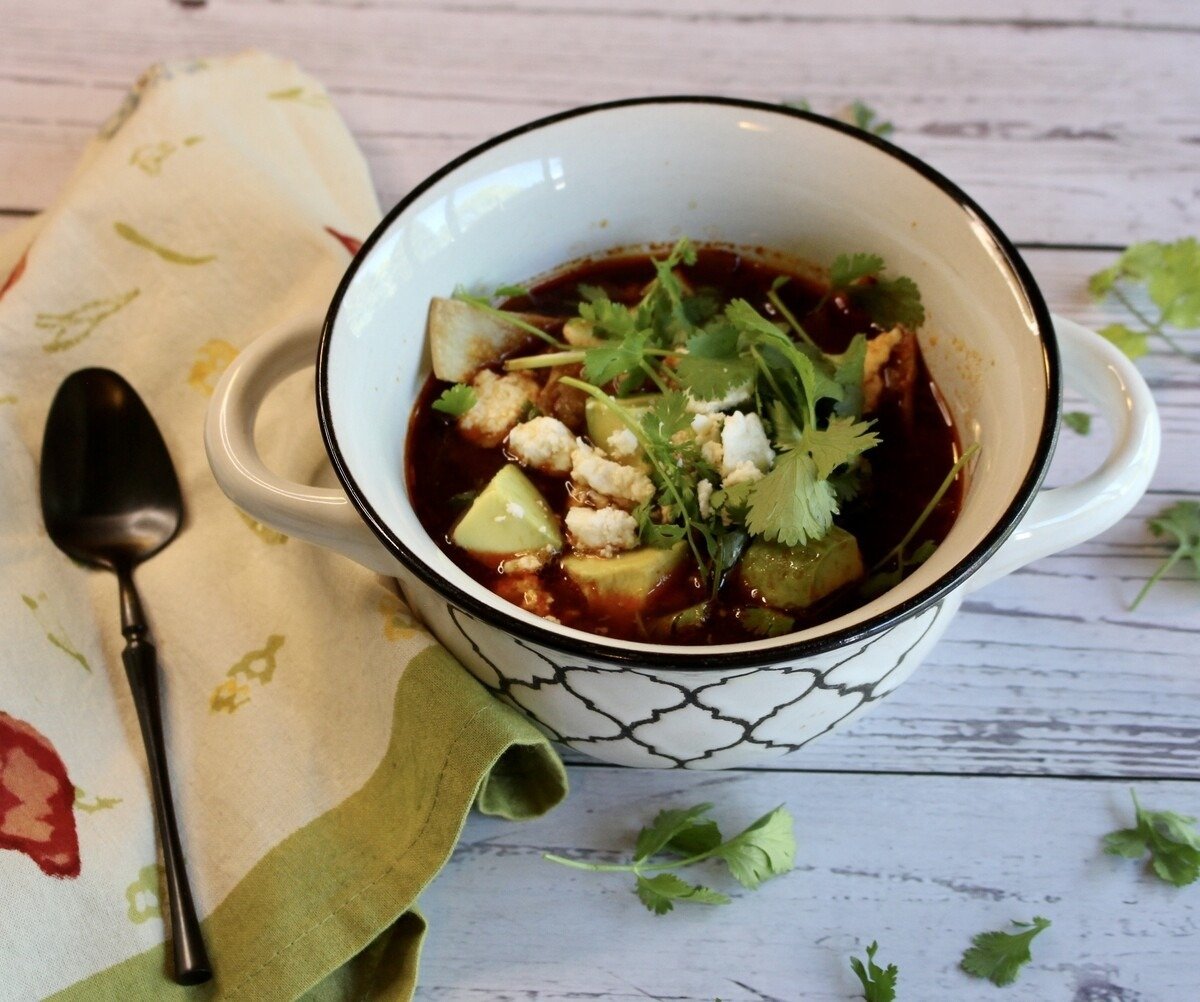 A bowl of tortilla soup with a napkin and a spoon.