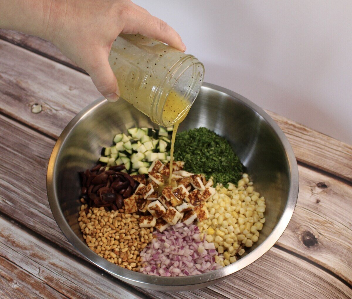 Farro, Corn, and Zucchini Salad with Fried Cheese in a bowl with dressing being poured over.