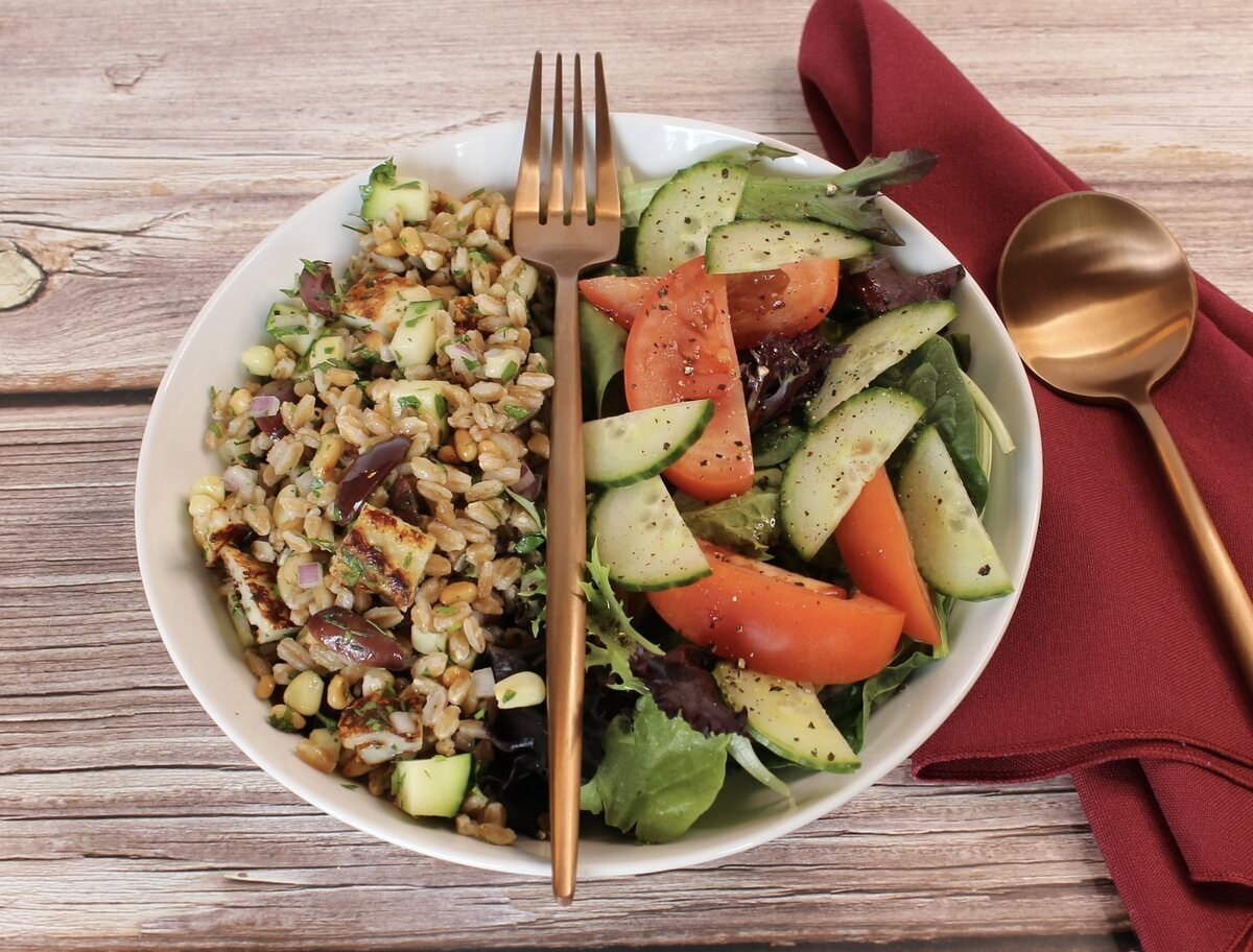 Farro salad in a bowl with a green salad and a fork laying through the middle.