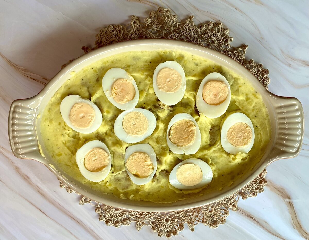 Mashed potatoes spread out in a dish with boiled egg halves tucked into the potatoes.