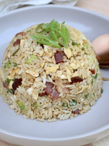 A dome shaped ball of fried rice on a plate with a spoon and garnished with green onions.