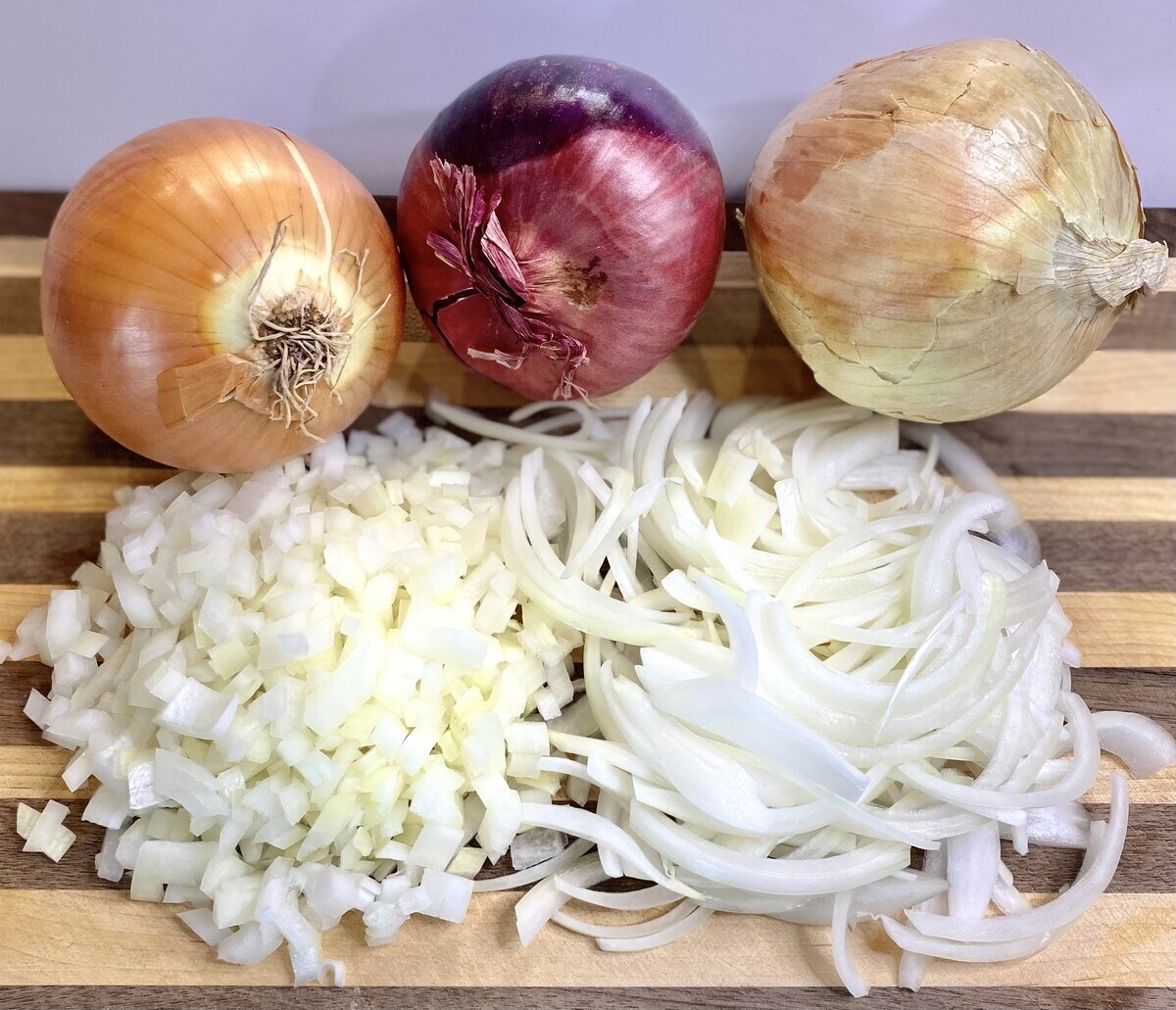 Three types of onions on a cutting board with diced and julienned onions.