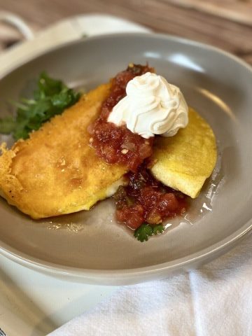 Two tacos on a plate with sour cream and salsa.