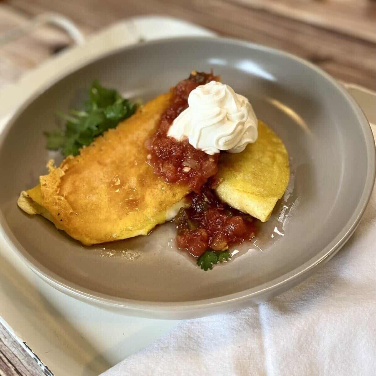 Two tacos on a plate with sour cream and salsa.