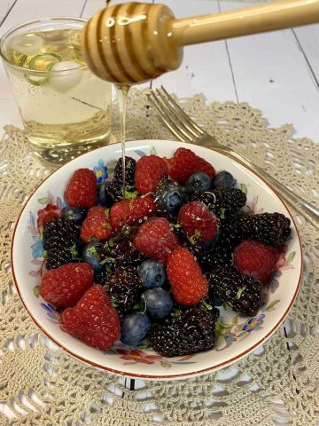 bowl of berries being drizzled with honey from a honey wand.