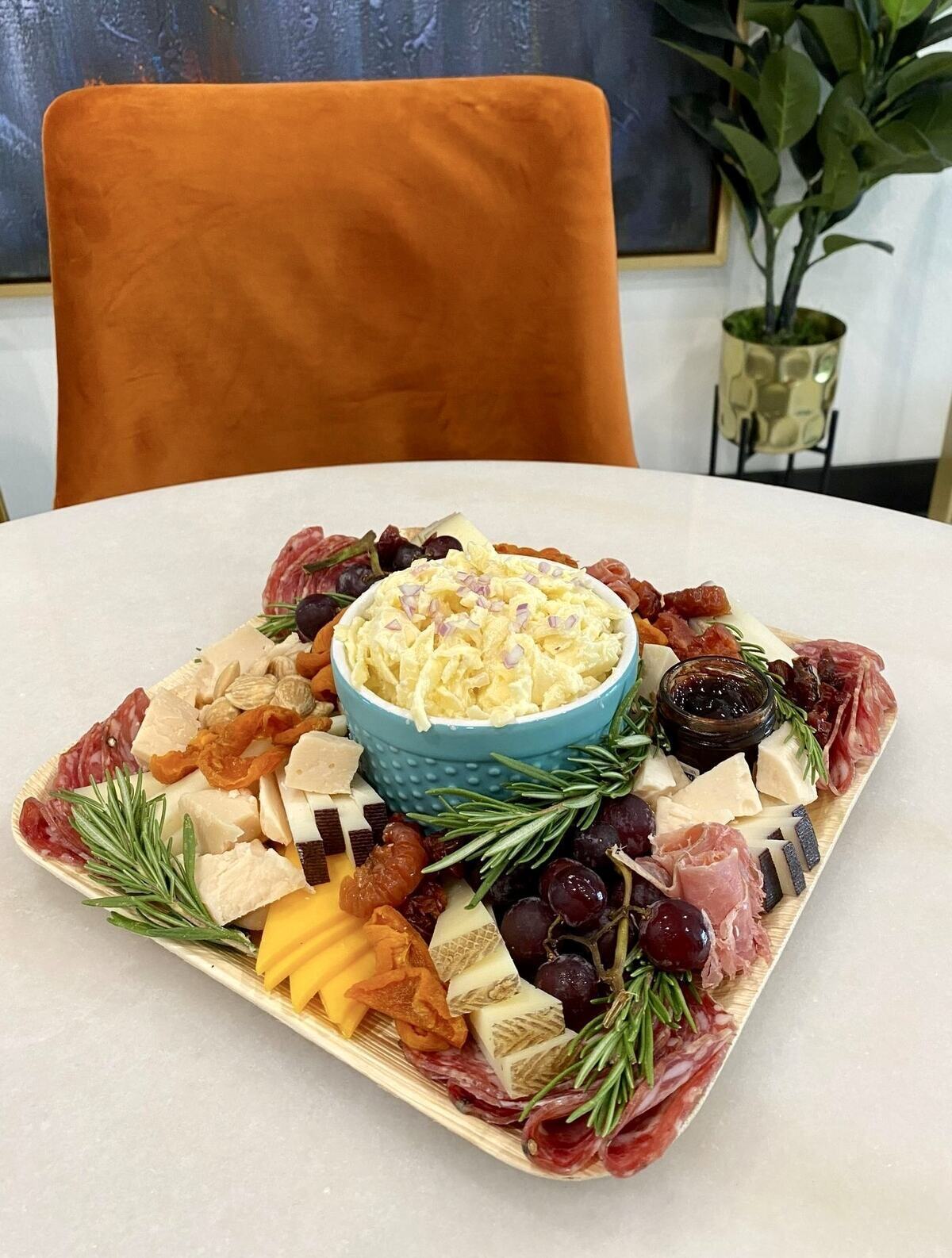 Cheese dip on a charcuterie plate with an orange chair behind it.