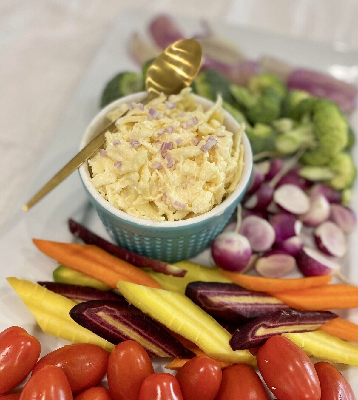 Cheese dip on a platter with crudite and a gold spoon.