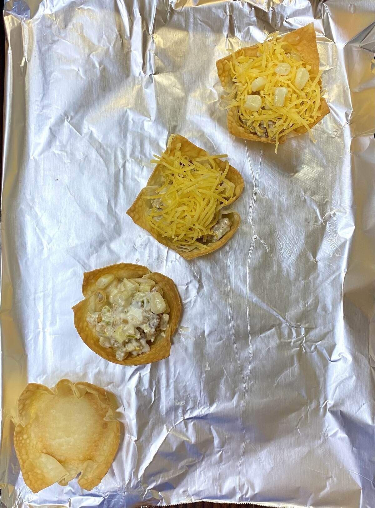 Wonton cups on a sheet pan in various stages of being filled and garnished.