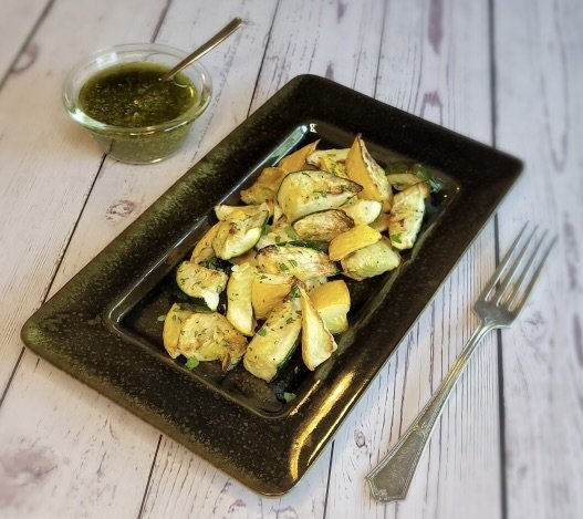 A plate of cooked squash with a fork and a side of italian salsa verde.