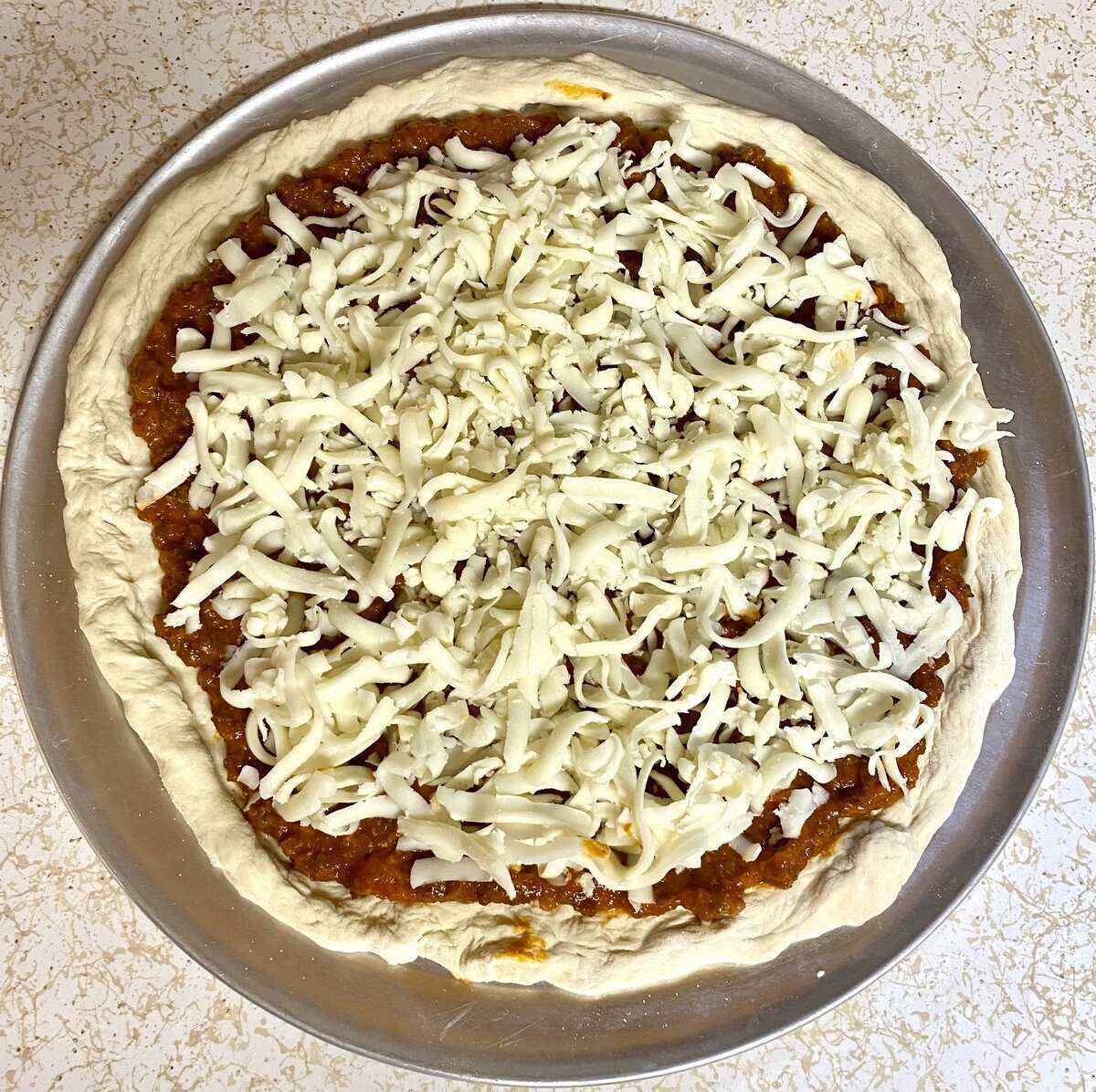 Cheese added on top of the bolognese sauce on the raw pizza dough.