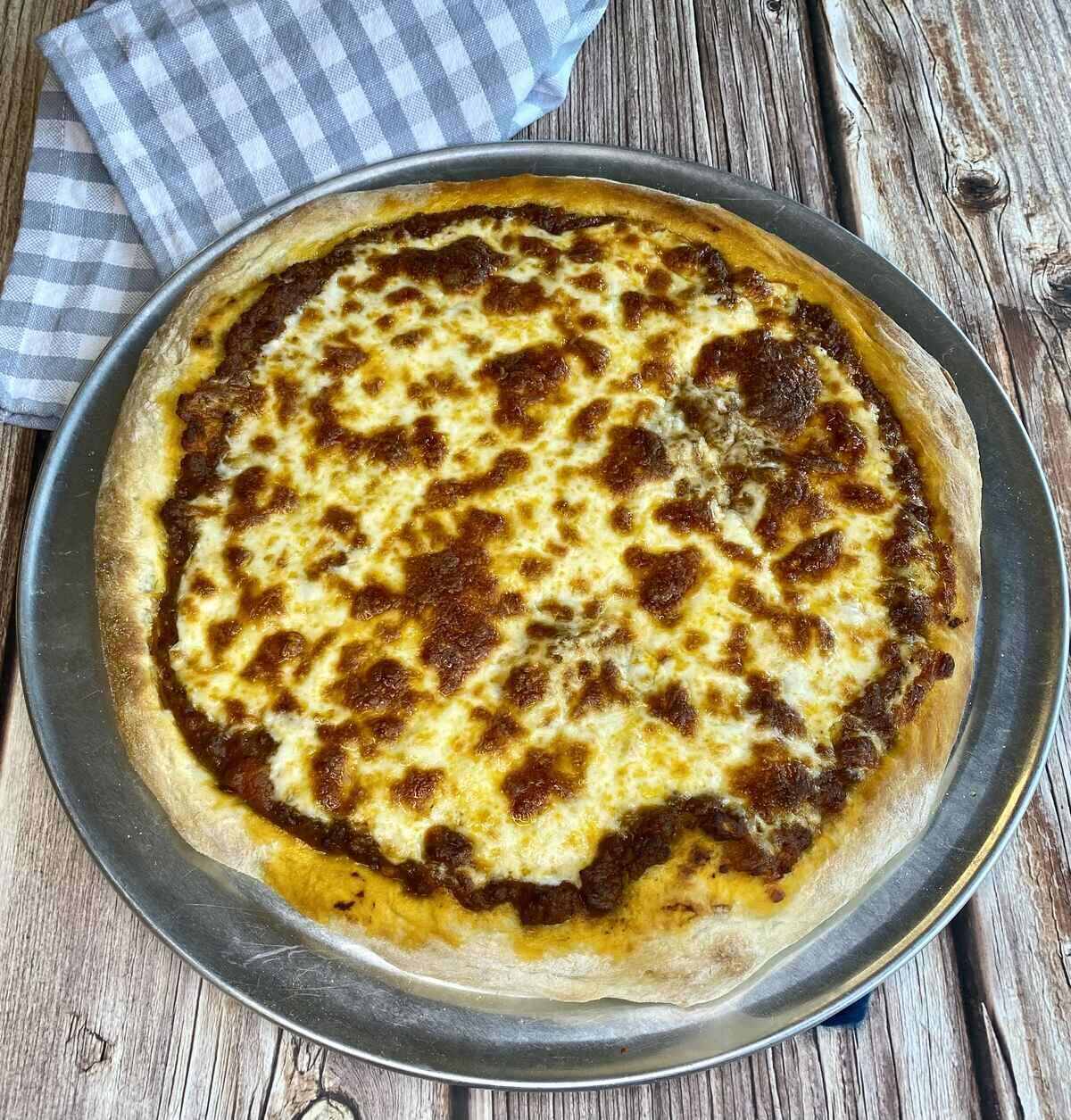 A fully cooked bolognese pizza on a pizza pan with a napkin.