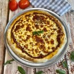 A bolognese pizza on a pizza pan with a napkin, tomatoes and basil alongside.