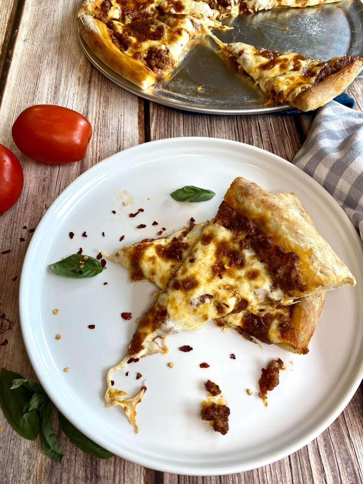 A few slices of pizza on a plate with red pepper flakes and the remaining pizza in the backgroung.