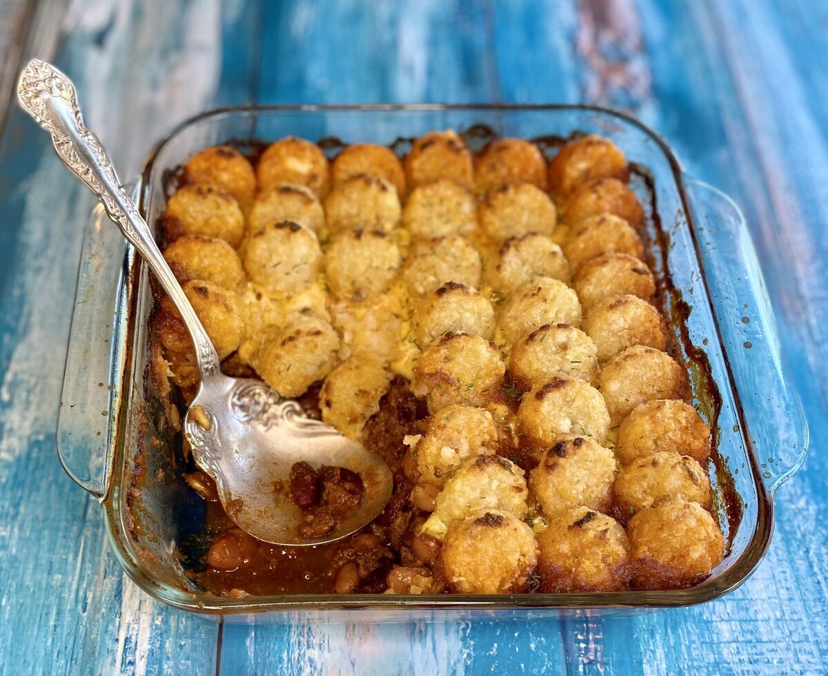 Baked chili tater tot casserole in a glass dish with a scoop taken out with a serving spoon.