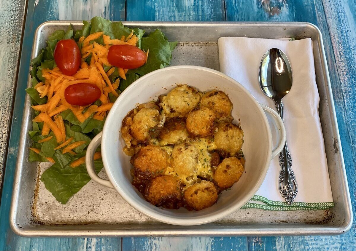 A metal tray holding a bowl of tater tot casserole beside a salad, napkin, and spoon.