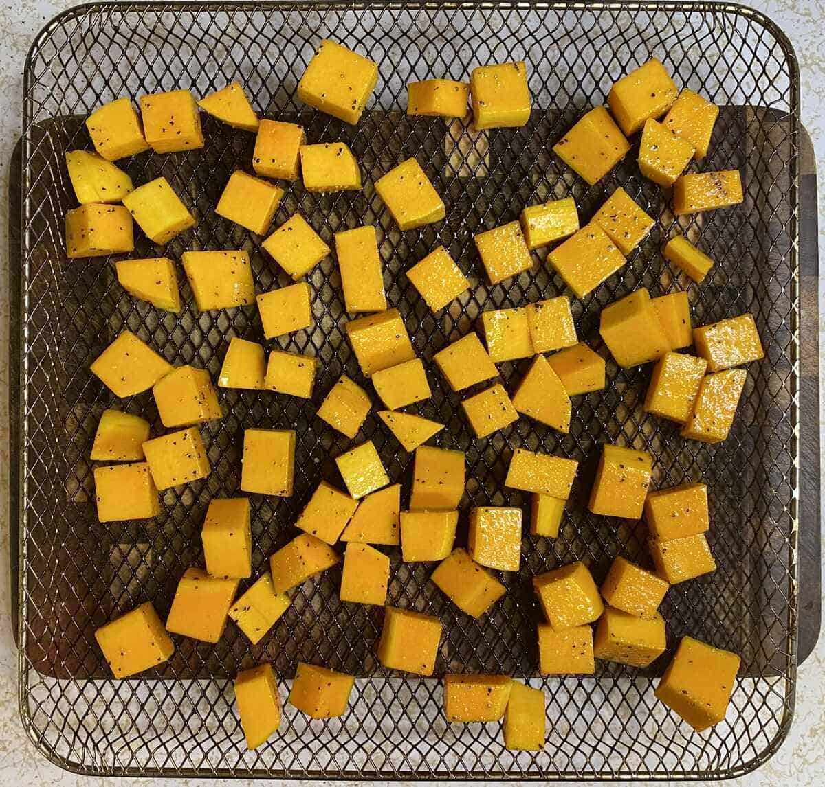 Butternut diced, oiled, seasoned, and spread out evenly in an air fryer basket.