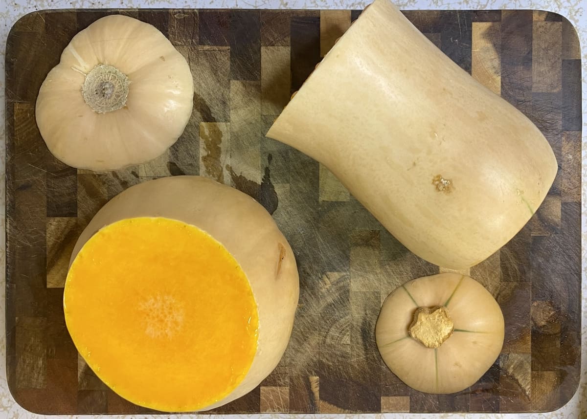 A butternut squash on a cutting board with the ends trimmed and the shaft separated from the bulb.