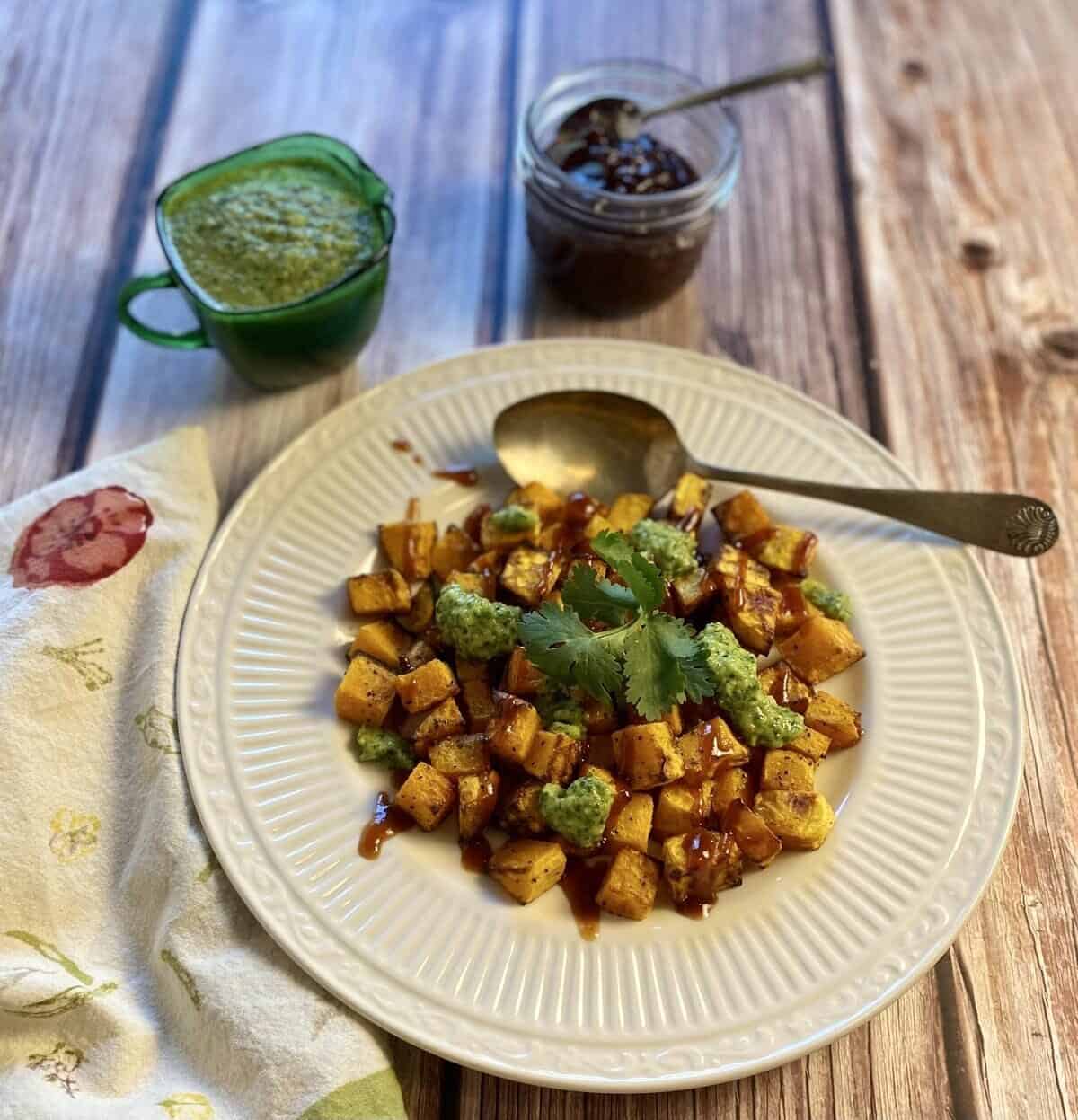 Air fryer butternut squash on a plate with both sauces and a cilantro garnish.