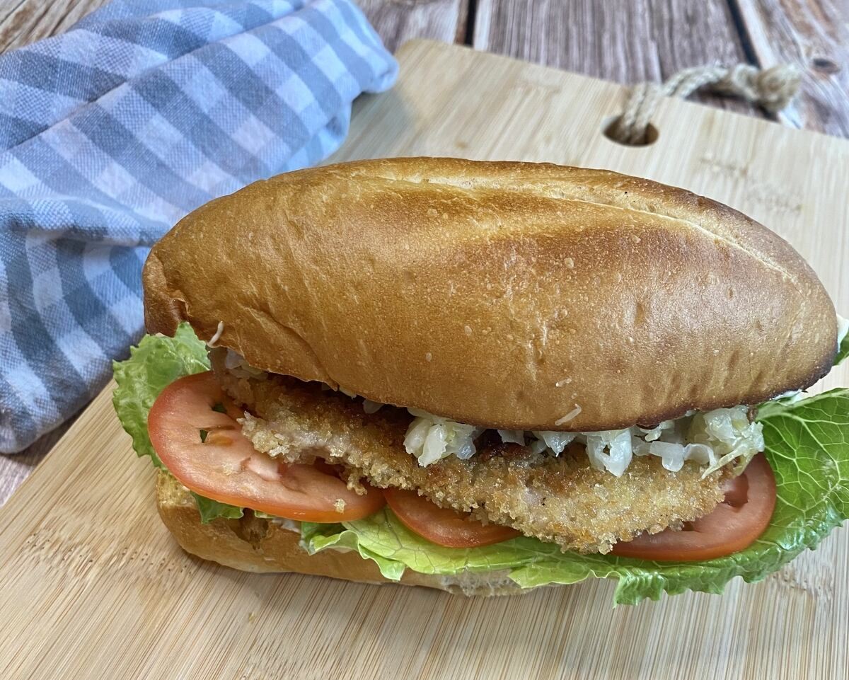 A whole pork schnitzel sandwich sitting on a cutting board.