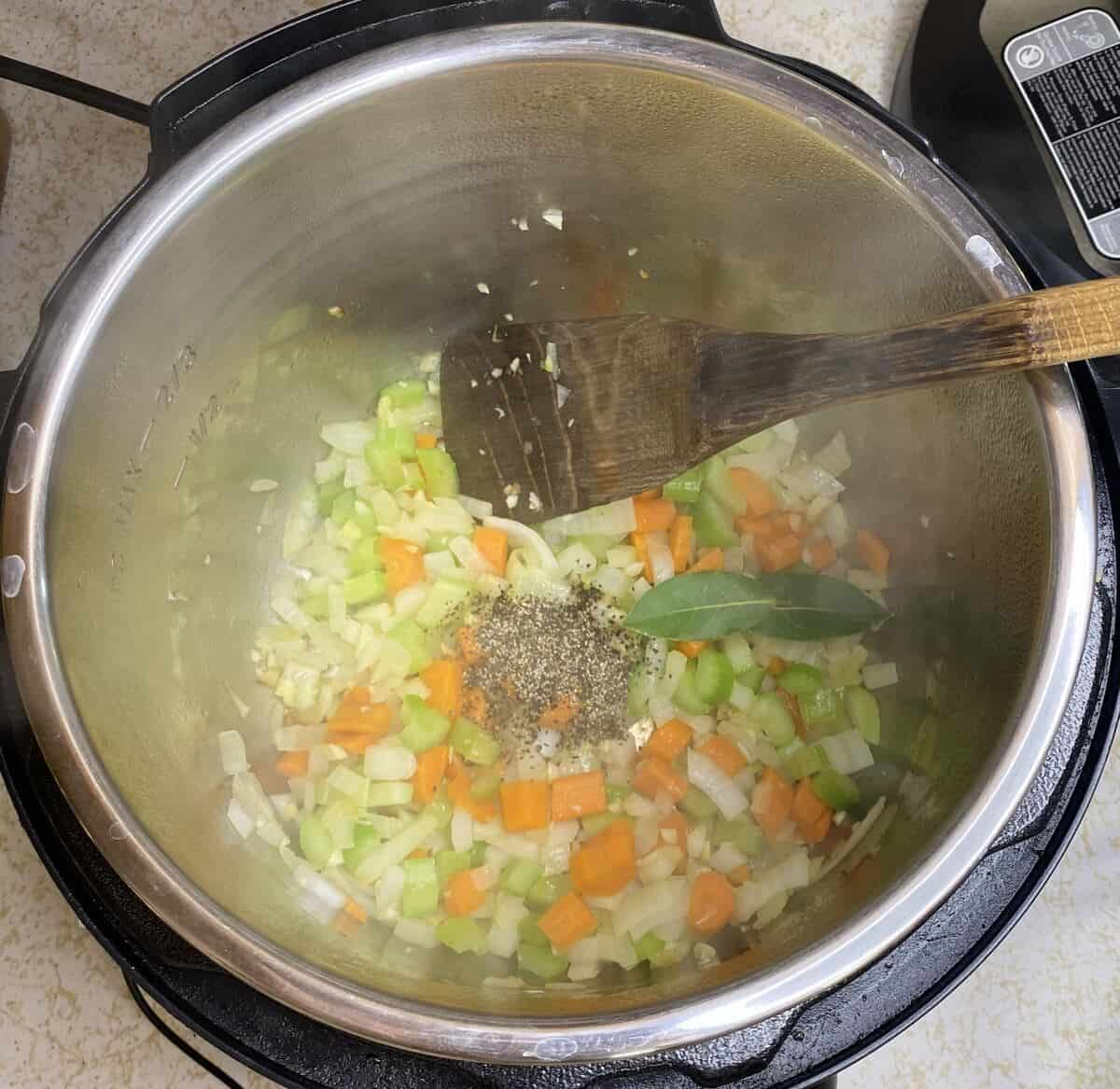 Showing the first step of sautéing the vegetables in the instant pot then adding pepper and by leaves.