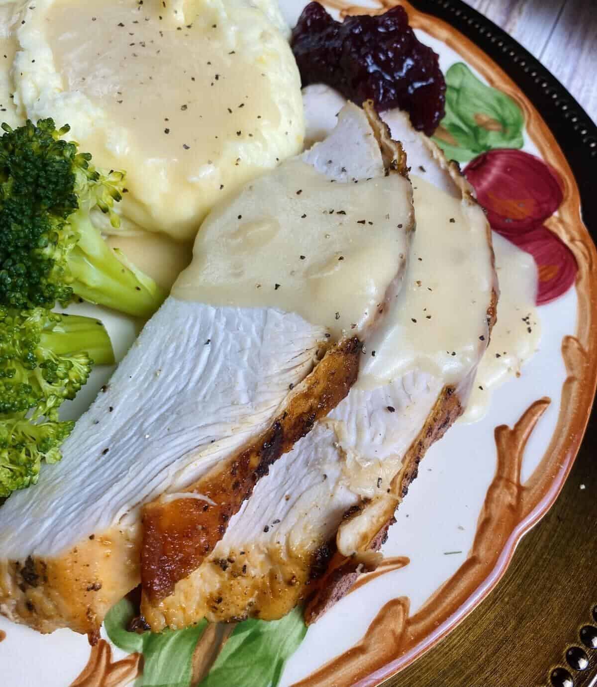 Closeup of slice turkey on a plate with gravy, potatoes, and broccoli.