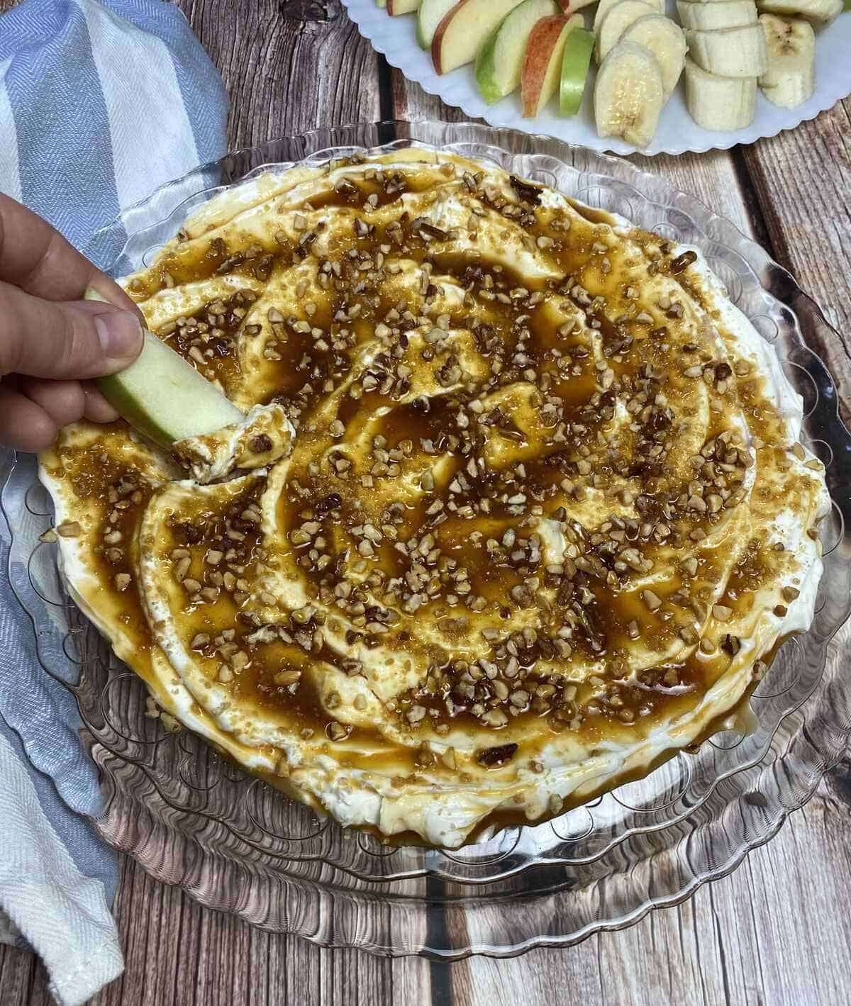 A hand spooning a bite of cheesecake dip with an apple slice.