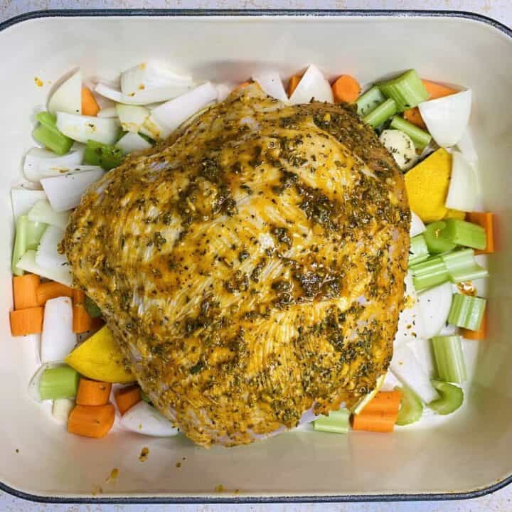 The roasting dish filled with vegetables and herbs with the raw buttered turkey placed on top.