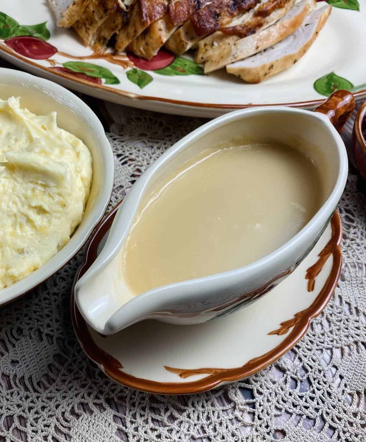 Easy turkey gravy in a boat alongside mashed potatoes and roasted turkey.