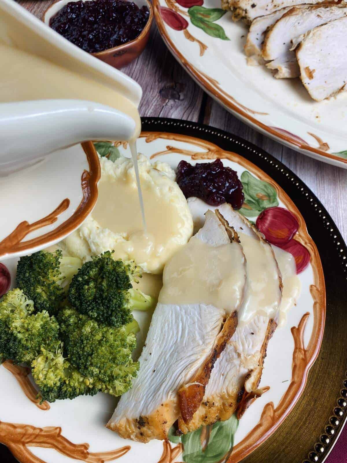 Pouring gravy from the boat onto a plate of mashed potatoes and roasted turkey.