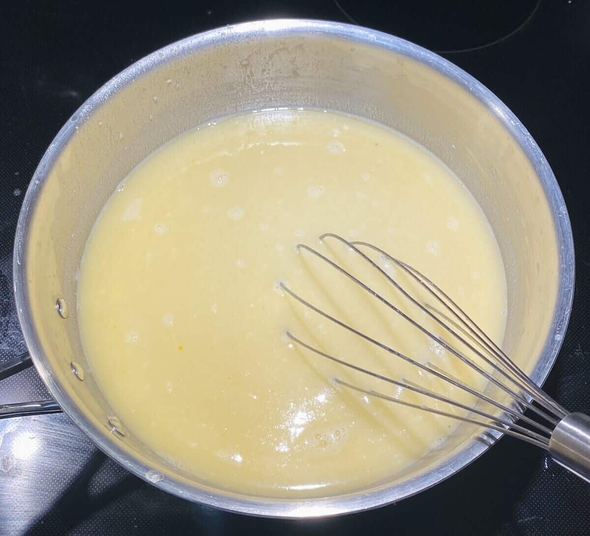 A pot on the stove with broth whisked into the roux.