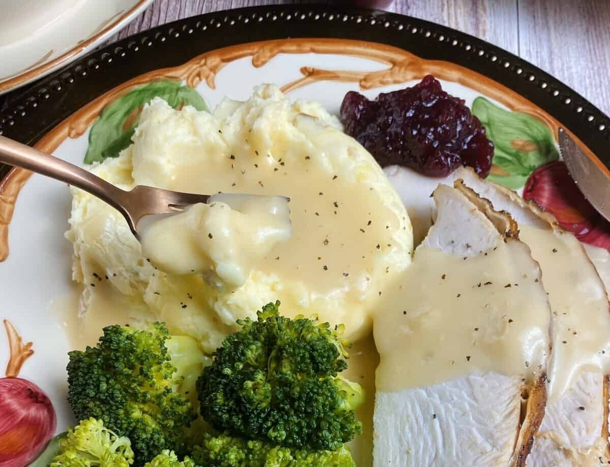 A fork pulling out a bite of mashed potatoes and gravy.