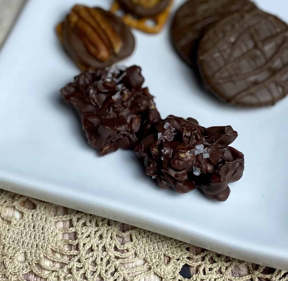 Chocolate cashew clusters with maldon flake salt on a white plate.