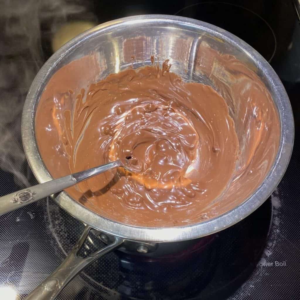 A double boiler on the stove with semi-sweet chocolate chips melting in the bowl.